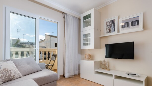 Una sala de estar moderna con sofá, televisor y balcón con vistas a edificios.