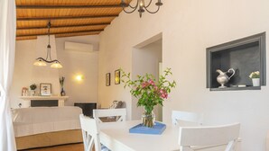 A dining area with a white table, chairs, and a vase with flowers. There is a chandelier above the table and a shelf with decorative items on the wall. - Can Clavell - Villa With Private Pool. Free Wifi (Colonia De Sant Pere (artà), Illes Balears)