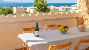 A table set with a bottle of wine, glasses, a fruit bowl, and a ceramic pot on a balcony overlooking a coastal view. - Can Clavell - Villa With Private Pool. Free Wifi (Colonia De Sant Pere (artà), Illes Balears)