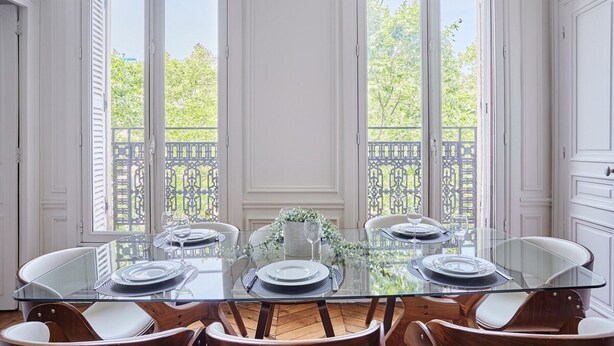A dining area with a glass table and wooden chairs, large windows with a view of a balcony and trees. - Magnificent Flat Centre de Paris Le Marais (Paris)