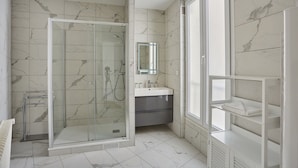 A modern bathroom with a glass-enclosed shower, a vanity with a mirror, and built-in shelving. - Magnificent Flat Centre de Paris Le Marais (Paris)