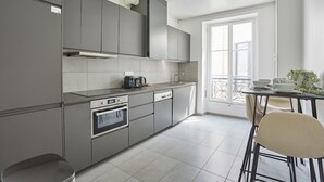 A modern kitchen with grey cabinets, a built-in oven, and a dining area with a table and chairs. - Magnificent Flat Centre de Paris Le Marais (Paris)