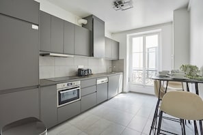 Une cuisine moderne avec des meubles gris, un four encastré et un coin repas comprenant une table et des chaises.