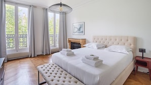 A spacious bedroom with a large bed, a fireplace, and a view of the outdoors through large windows. - Magnificent Flat Centre de Paris Le Marais (Paris)