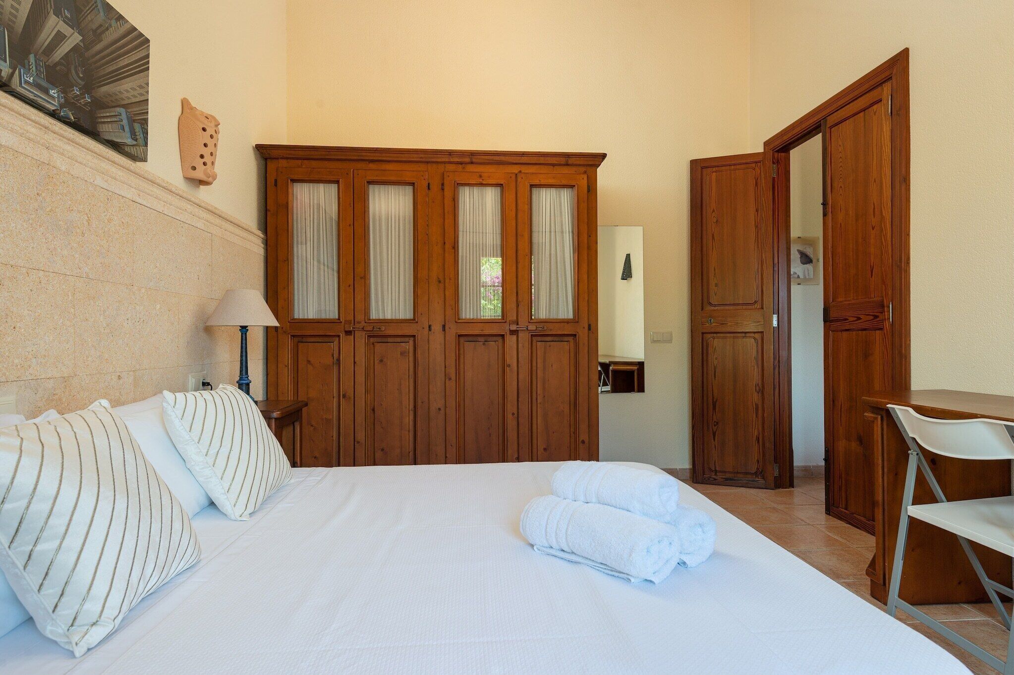 Ein Hotelzimmer mit einem großen Bett, zwei Nachttischen, einem Holzschrank, einem Schreibtisch und einem Stuhl.