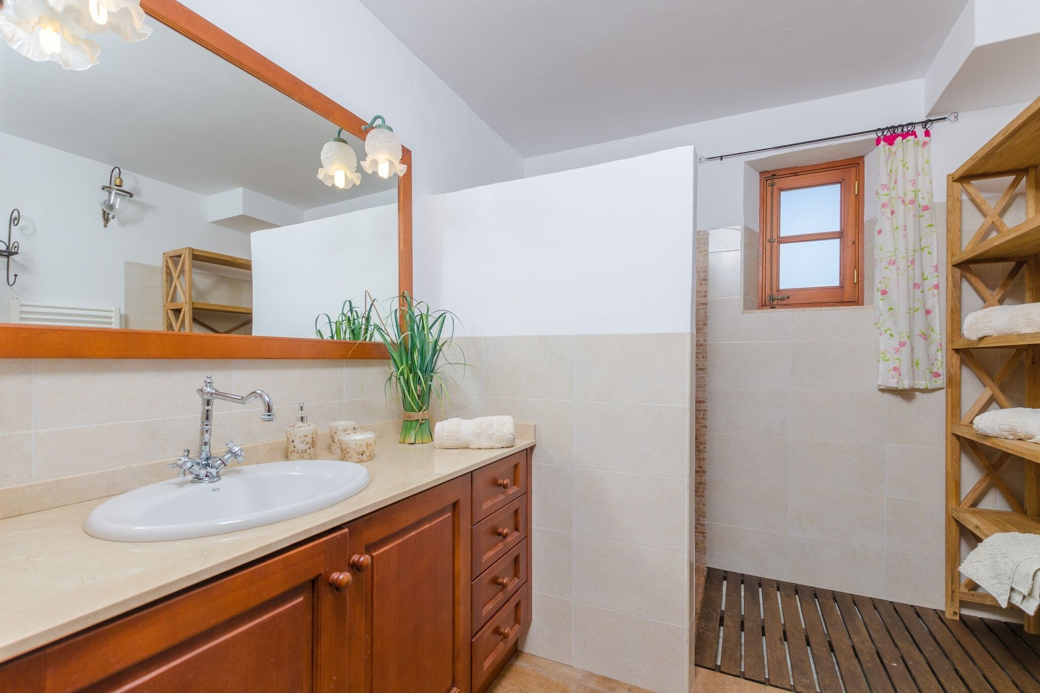 Ein Badezimmer mit Waschbecken, Spiegel, Holzsärchen und Duschbereich mit Fenster und Handtuchhalter.