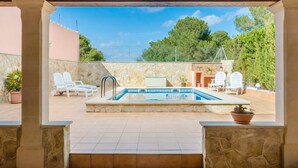 An outdoor swimming pool with lounge chairs and a stone wall, surrounded by greenery and a clear sky. - Villa Gloria - Villa With Private Pool In Cala Pi (Cala Pi , Illes Balears)