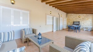 A spacious outdoor patio with wicker furniture, a glass-top table, and a stone wall backdrop. - Villa Gloria - Villa With Private Pool In Cala Pi (Cala Pi , Illes Balears)