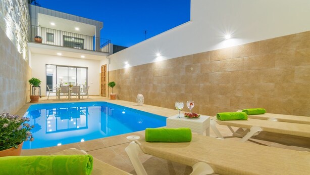 A modern pool area with lounge chairs and a table, surrounded by a stone wall and a balcony.