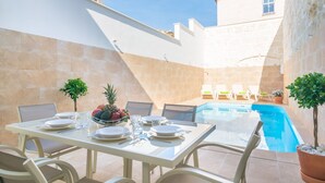 A dining area with a pool, white walls, and a stone building in the background.