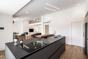 A modern kitchen with a large island, a dining area with a wooden table, and a staircase leading to an upper level.