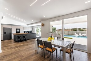 A modern kitchen with a central island, a dining area with a table and chairs, and a view of an outdoor swimming pool.