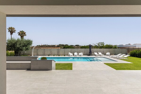 A modern outdoor pool area with a clear blue pool, white lounge chairs, and a view of the surrounding landscape.