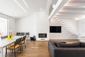 Un salon moderne comprenant un canapé, une table à manger, des chaises, un téléviseur et un escalier.