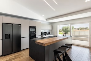 A modern kitchen with a central island, stainless steel appliances, and a large window providing a view of the outdoors.
