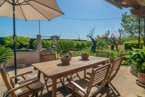 An outdoor patio with a wooden table and chairs, surrounded by potted plants and a large umbrella. - Can Pilos - Apartment In Inca. Free Wifi (Inca, Illes Balears)