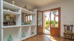 Ein Zimmer mit weißen Regaleinheiten, die verschiedene dekorative Gegenstände zeigen, einer Holztür, die zu einem Außenbereich führt, und einem Stuhl in der Nähe der Tür.