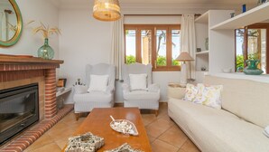 Ein Wohnzimmer mit Kamin, zwei Sesseln, einer Couch, einem Holztisch und einer Pendelleuchte.
