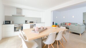 A modern kitchen with white cabinetry, a microwave, oven, and a dining area with a wooden table and white chairs. - Na Valenta - Villa With Private Pool In Artà (Artà, Illes Balears)