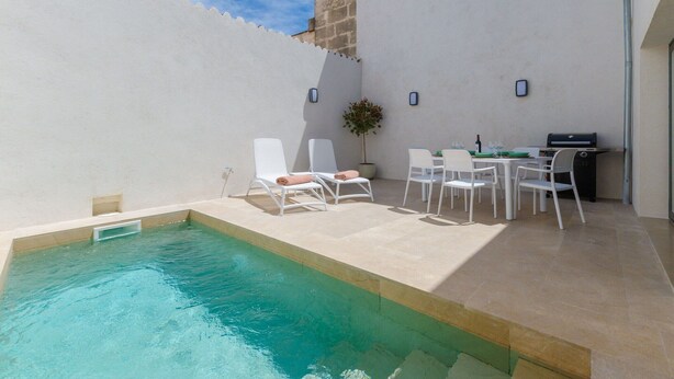 A swimming pool with white lounge chairs and a table with chairs, surrounded by a white wall and a stone building in the background. - Na Valenta - Villa With Private Pool In Artà (Artà, Illes Balears)