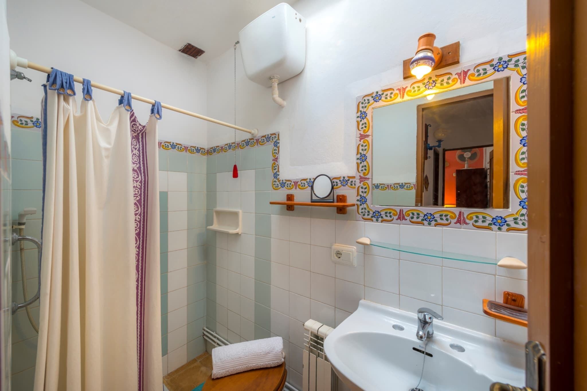Ein Badezimmer mit Dusche, Toilette, Waschbecken und einem Spiegel mit dekorativen Fliesen.