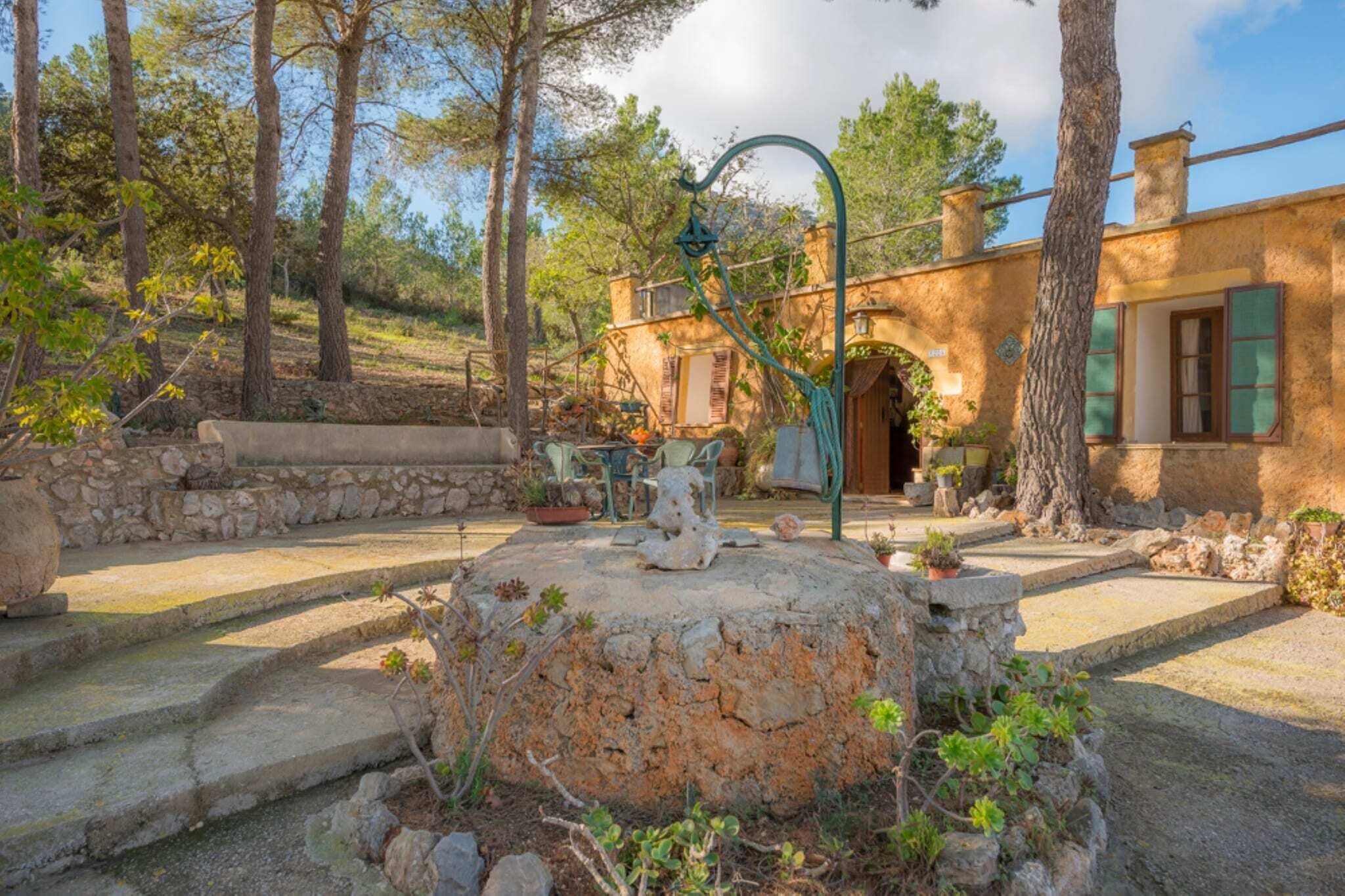 A rustic stone fountain in a garden with a stone wall and steps leading to a wooden door.