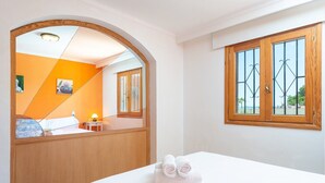 A hotel room with a bed, a wooden headboard, a window with metal bars, and a view of the outside. - Bellavista - Apartment In Port D'alcúdia (Port D'alcudia, Illes Balears)