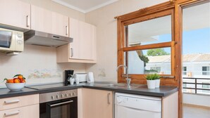 A modern kitchen with light-colored cabinets, a built-in oven, a dishwasher, and a window with a view of buildings. - Bellavista - Apartment In Port D'alcúdia (Port D'alcudia, Illes Balears)