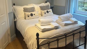 A neatly made bed with white linens and patterned pillows, a wooden floor, and a window with curtains.