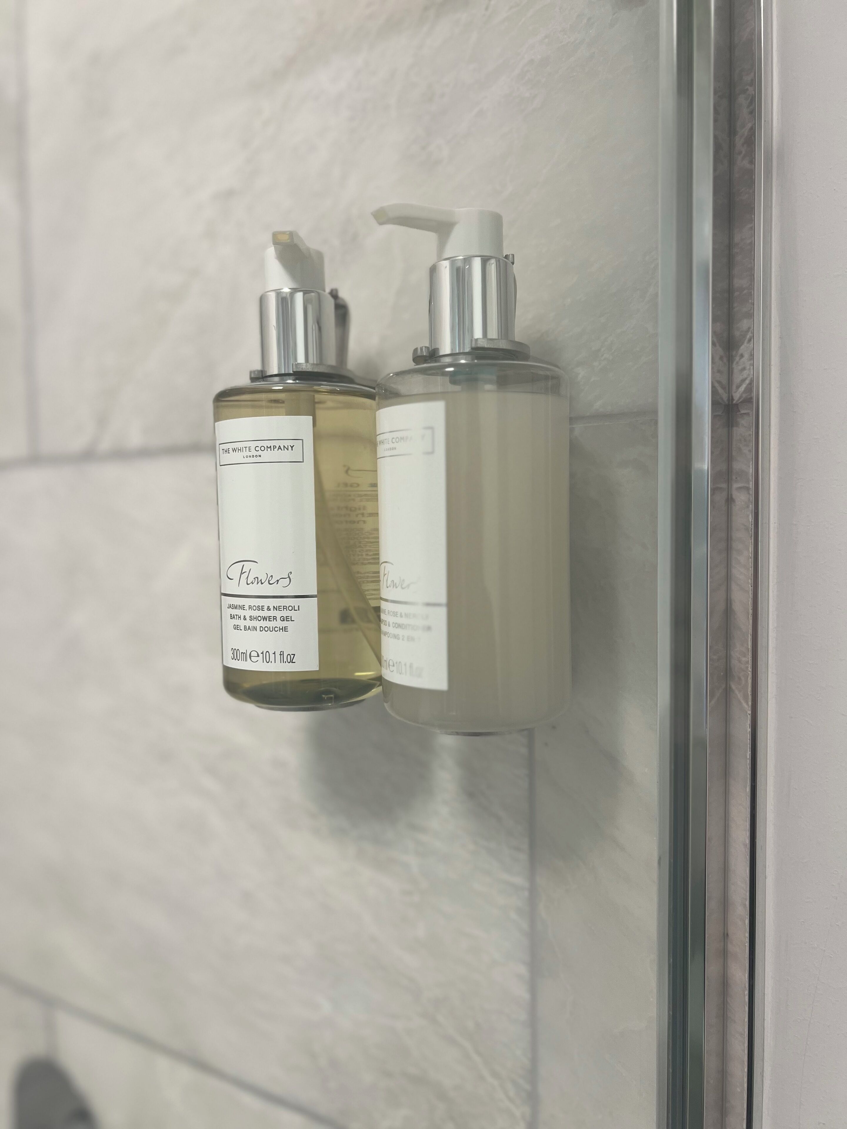 Two bottles of The White Company bath and shower gel on a bathroom wall.
