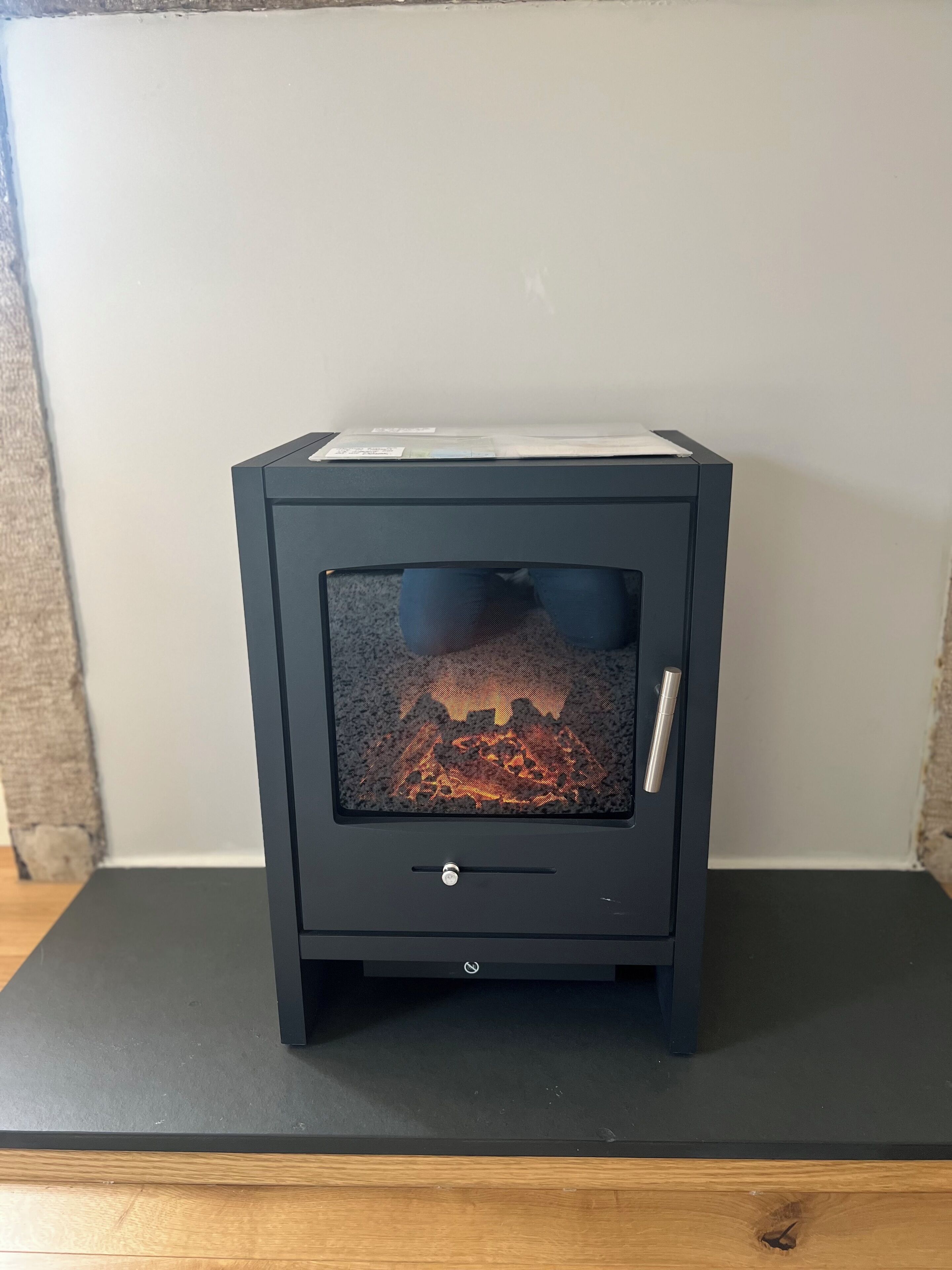 Ein schwarzer Kaminofen mit Glasfront, einer Bedieneinheit und einem Metallgriff.