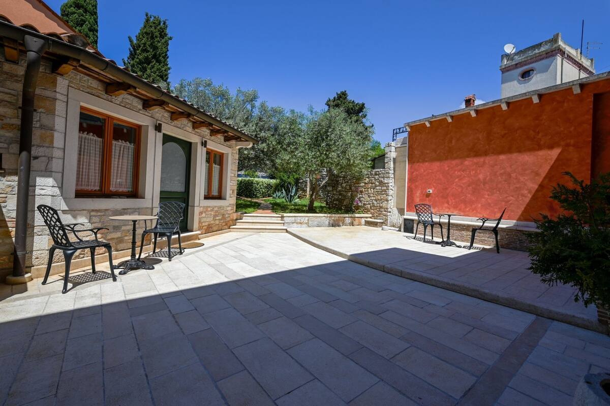 Un cortile con pavimento in pietra, posti a sedere all'aperto e un edificio in pietra con un muro rosso.
