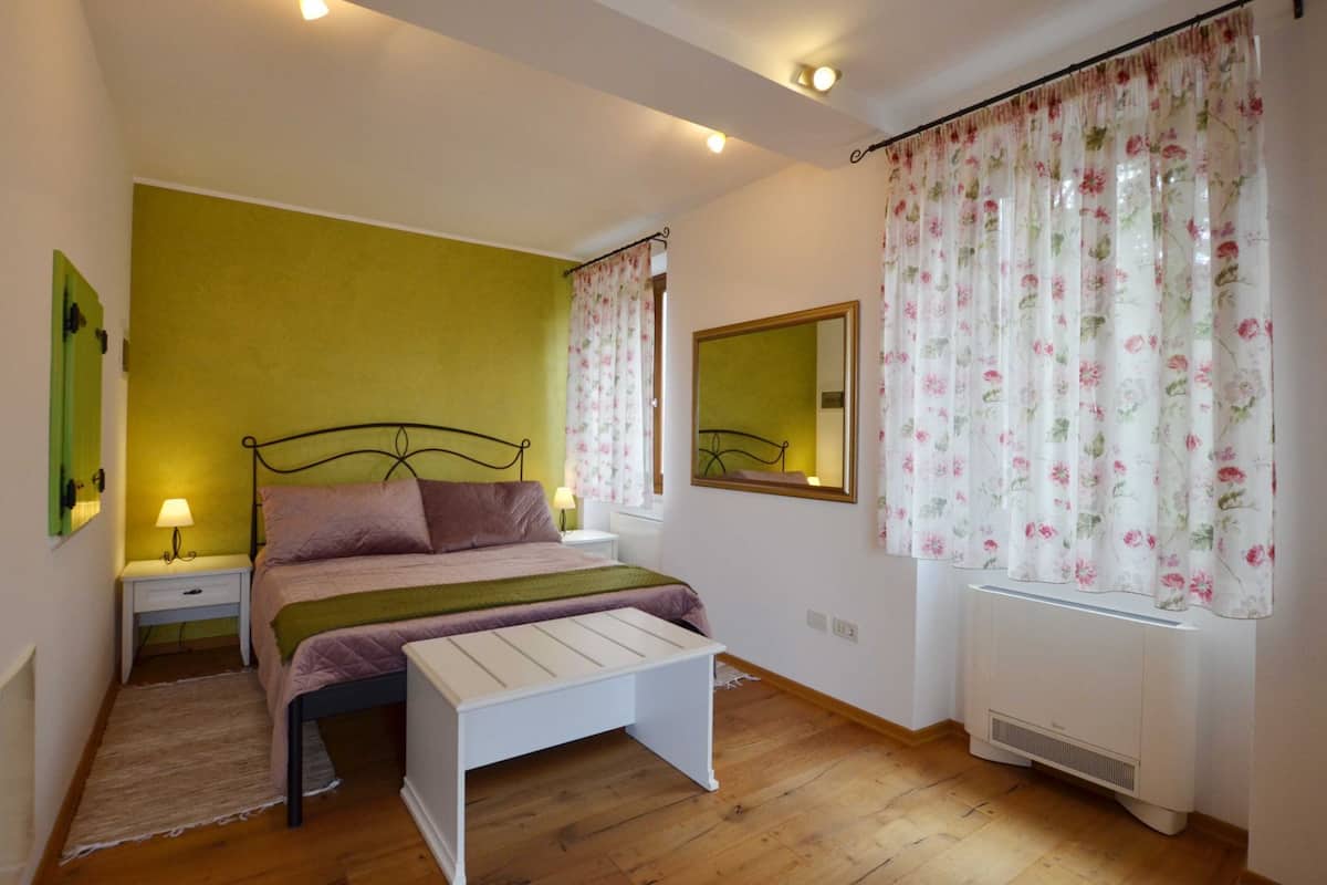 Una camera da letto con un letto, comodini, una panca, uno specchio e una finestra con tende floreali.