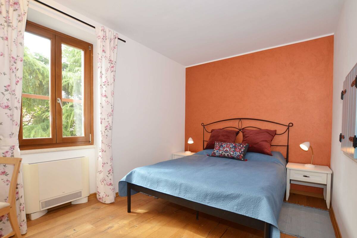 Una camera da letto con un letto, due lampade da comodino, una finestra con tende, un termosifone e un pavimento in legno.