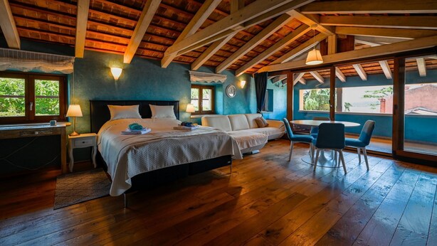 A bedroom with a wooden ceiling, a bed, a sofa, a desk, and a dining area with chairs. - Georgeous and Warm Living Downtown Rovinj (Rovinj)