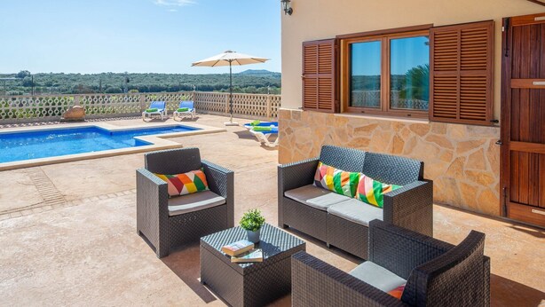 Une terrasse dotée de meubles en osier, une piscine et une vue sur la campagne.