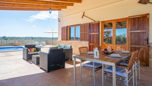 Une terrasse extérieure avec une piscine, des meubles en osier, une table en bois dressée pour les repas et une vue sur le paysage.
