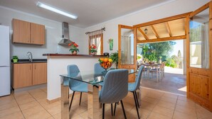 Une cuisine moderne avec des meubles en bois, une table à manger en verre et des chaises. On peut admirer, depuis la cuisine, un patio extérieur avec une table à manger et des chaises.