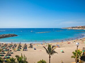 A beach with umbrellas, people, and a clear blue sky.