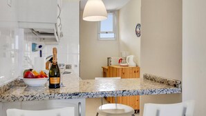 A modern kitchen with a marble countertop, white chairs, a bottle of Canti champagne, and a fruit bowl. - El Sol del Sur, Ocean View, 2 Pool, Fiber (Costa Adeje)