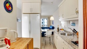 A compact kitchen with white cabinets, a wooden countertop, a built-in oven, and a dining area with a blue sofa. - El Sol del Sur, Ocean View, 2 Pool, Fiber (Costa Adeje)