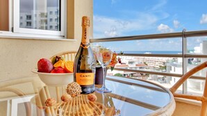 A bottle of Canti Prosecco DOC, a bowl of fruit, and a glass on a balcony table with a view of buildings and the sea. - El Sol del Sur, Ocean View, 2 Pool, Fiber (Costa Adeje)