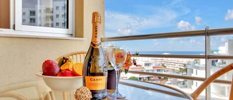 A bottle of Canti Prosecco DOC, a bowl of fruit, and a glass on a balcony table with a view of buildings and the sea.