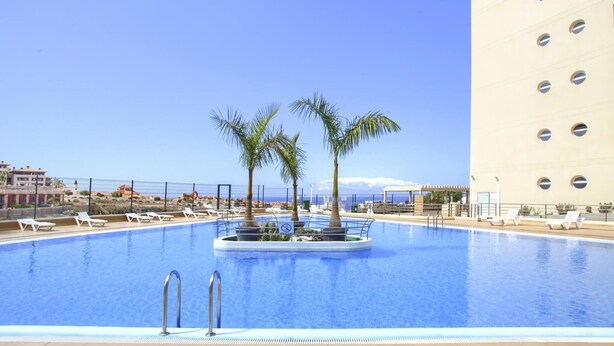 A swimming pool with lounge chairs, palm trees, and a view of the ocean. - El Sol del Sur, Ocean View, 2 Pool, Fiber (Costa Adeje)