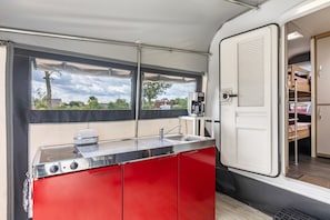 Cocina compacta con estufa de acero inoxidable, un lavamanos y ventana con vista a un barrio residencial.