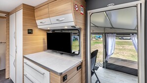 A compact RV interior with a kitchenette, a flat-screen TV, and a sliding door to the outside. - Caravan 'Max 2 Erw Und 2 Kd' with Shared Garden and Wi-Fi (Zeschdorf)