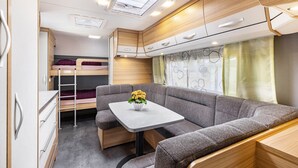 A compact RV interior with a bunk bed, a dining area with a table, and a kitchenette. - Caravan 'Max 2 Erw Und 2 Kd' with Shared Garden and Wi-Fi (Zeschdorf)
