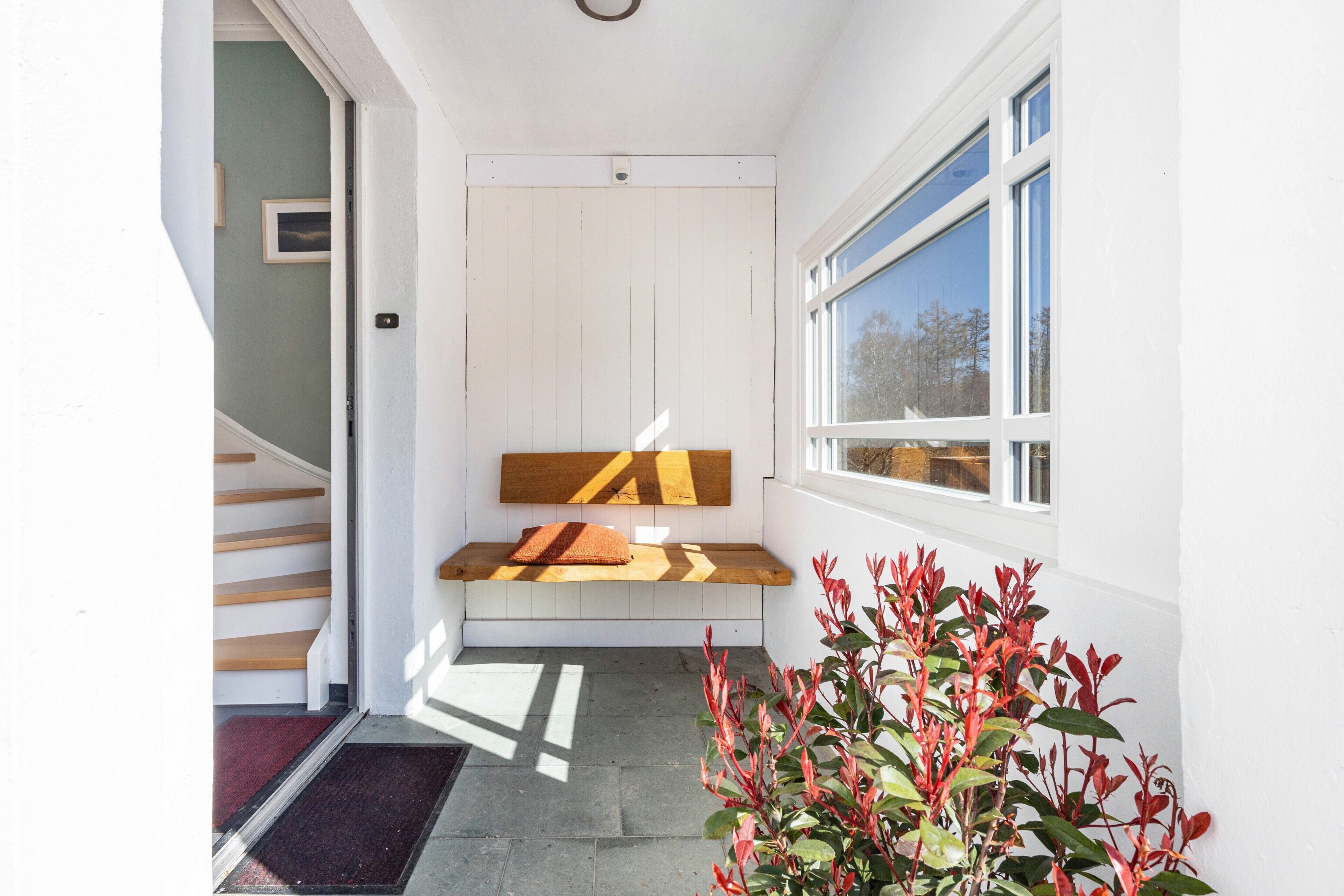 Un couloir avec un banc en bois, une porte et une fenêtre.