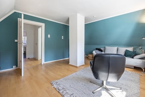 A modern living room with teal walls, a grey sofa, a black chair, and a wooden floor.