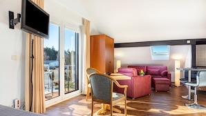Une chambre d’hôtel moderne dotée d’une grande porte-fenêtre coulissante, d’un téléviseur à écran plat, d’un canapé rouge, d’une table à manger avec des chaises et d’un petit balcon.